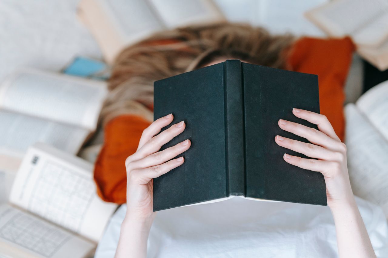 The Art of Drawing Readers In: Your attractive post title goes here From above of unrecognizable female reading black book with hardcover while lying on floor near various literature in light room